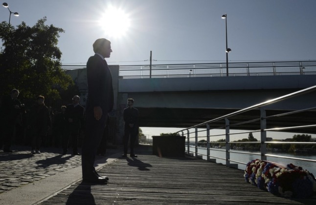 French President Emmanuel Macron stands to attention after laying a wreath near the Bezons bridge in Colombes, near Paris