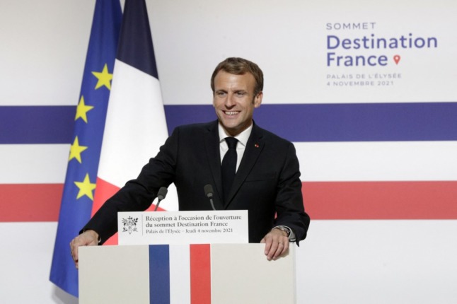 France's President Emmanuel Macron smiles while standing at a podium giving a speech at the opening of the Destination France summit
