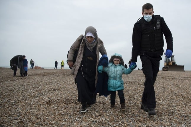 A member of the UK Border Force (R) helps people on a beach in Dungeness