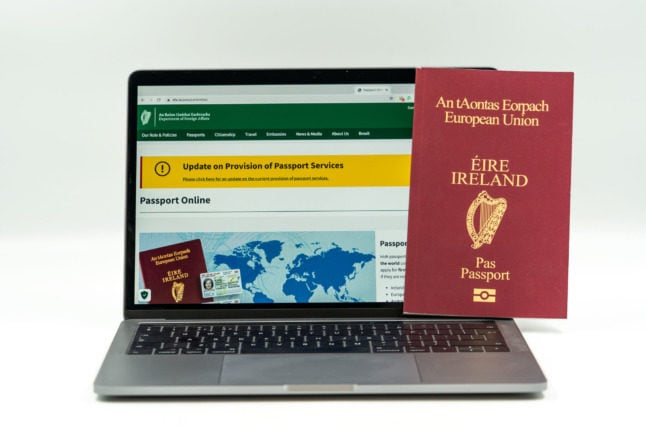 A laptop is displaying the online application for the Irish passport with an Irish passport replica stood up right, next to the screen.