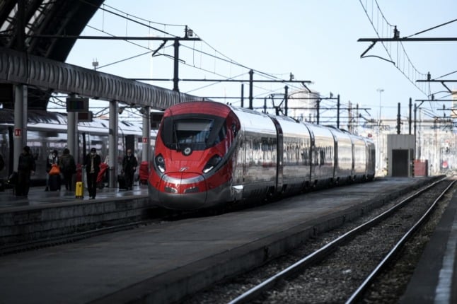 A bright red high-speed train pulls into a railway station