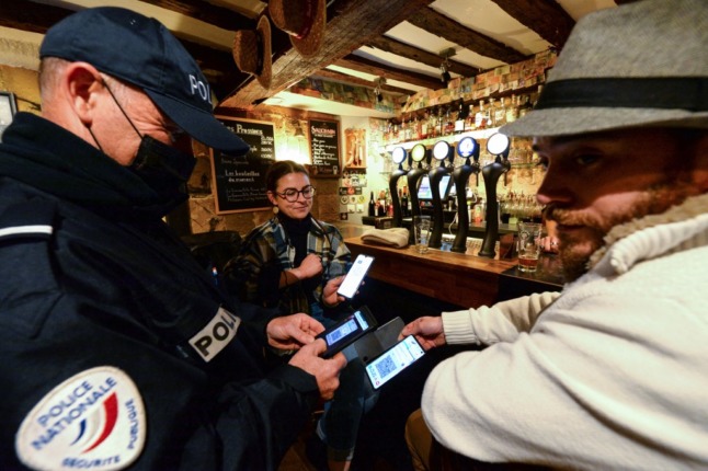 A policeman checks the Covid-19 health pass of customers in a bar in France. 