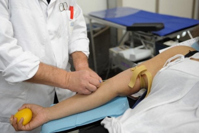 A medical professional prepares to insert a needle into the arm of a blood donor
